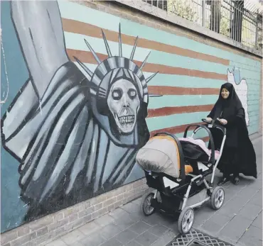  ??  ?? An Iranian woman walks past graffiti on the walls of the former US embassy in Tehran