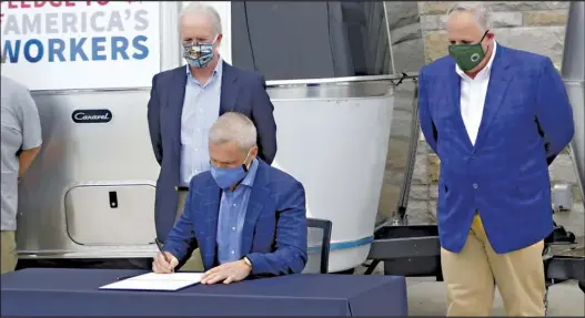  ??  ?? Airstream CEO Bob Wheeler signs the pledge while U. S. Secretary for the Interior David Bernhardt and Mark Seery watch. The signing came after they toured the Jackson Center company .