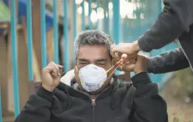  ??  ?? Moses helps Juan Rodriguez fit a smoke mask to protect his lungs in the smoky air. The organizati­on Mask Oakland is giving away thousands of masks.