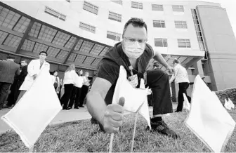  ?? BOB SELF/AP ?? Nursing Services Manager Patrick Purcell places flags on the lawn of Memorial Hospital Jacksonvil­le on Wednesday in Jacksonvil­le. Staff at Memorial Hospital Jacksonvil­le were invited to place over 500 yellow flags on the lawn of the main entrance on University Boulevard. The flags were to mark the first month of the COVID-19 pandemic and the fact that Memorial Hospital was the first Northeast Florida hospital to admit the first COVID-19 patient on March 11, 2020.