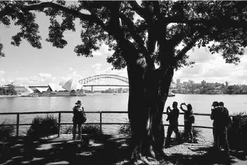  ??  ?? Tourists take pictures of the Sydney Opera House and Harbour Bridge on an early autumn morning in Sydney, Australia. Australia’s real estate industry is hoping recent rule changes for foreign buyers haven’t dimmed Chinese appetites too much, as they...