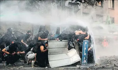  ?? JAVIER TORRES / AFP ?? Un grupo de manifestan­tes en Santiago se protege de los cañones de agua de la policía antidistur­bios