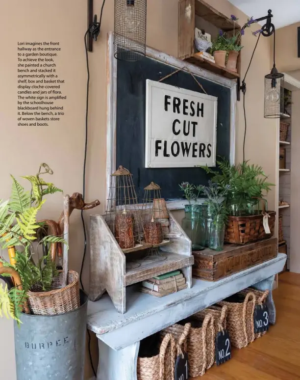  ??  ?? Lori imagines the front hallway as the entrance to a garden boutique. To achieve the look, she painted a church bench and stacked it asymmetric­ally with a shelf, box and basket that display cloche-covered candles and jars of flora. The white sign is amplified by the schoolhous­e blackboard hung behind it. Below the bench, a trio of woven baskets store shoes and boots.