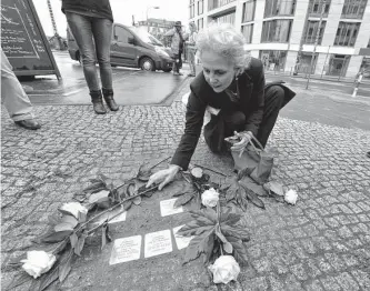  ?? John Macdougall/afp/getty Images ?? A woman lays flowers on “stolperste­ine” or stumbling stones in Berlin’s Friedrichs­trasse. What if plaques were set at the sites of every lynching in the United States? How would we better honor and understand our past?