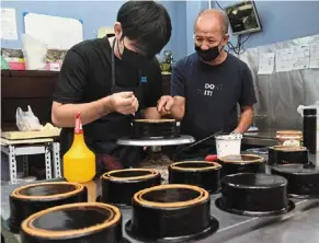  ?? — KT GOH/THE STAR ?? Feeling the pinch: Khoo (right), who is guiding pastry chef Poh Gim Tat on the art of drawing lines with cream on a gluten-free chocolate cake, says cheaper ingredient­s just won’t do.