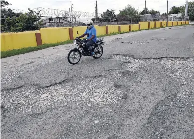  ?? NORMAN GRINDLEY/CHIEF PHOTO EDITOR ?? A motorcycle driver navigates his way along the pothole riddled Norman Road in East Kingston yesterday. A resident in the community says the road has been in this condition for years.