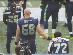  ?? The Associated Press ?? Seattle Seahawks center Justin Britt (68) and cornerback Jeremy Lane (20) stand near defensive end Michael Bennett (72) as Bennett sits on the bench during the national anthem before Friday’s preseason game against the Minnesota Vikings.