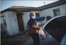  ?? WONG MAYE-E / AP ?? Norma Flores carries groceries into her home last month in Henderson. Flores is a Mexican immigrant who spent two decades working as a waitress at Fiesta before COVID-19 descended and she lost her job.
She lives in a concrete block house with six grandchild­ren, most of them attending school online. She dreads when she overhears a teacher asking what students had for their lunches and snacks. She rarely has enough food for both.