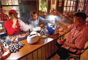  ?? BAY ISMOYO/AFP ?? E-cigarette cafe employees (left) vape with customers in Jakarta.