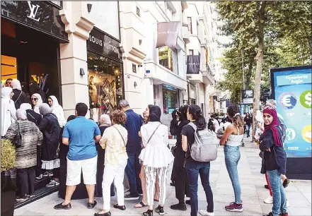  ??  ?? Tourists, many from Saudi Arabia and Asia, queue outside a luxury brand Louis Vuitton store next to a billboard giving currencies rates in Istanbul on Aug 13. The collapse of the Turkish lira has caused trauma as Turks see their purchasing power reduced but has been an unexpected windfall for foreign tourists visiting the country at the peak of the summer season. Tourists, mainly from Saudi Arabia and Asia, formed long queues outside luxury brand design stores like Louis Vuitton, Chanel and Prada when the Turkish currency took a severe hit against dollar, falling over 16 percent on its value on Aug10. (AFP)