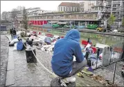  ?? THIBAULT CAMUS / AP ?? Migrants sit beside a makeshift camp Thursday in Paris. President Emmanuel Macron’s government is ramping up expulsions, raising pressure on economic migrants and allowing ID checks in emergency shelters.