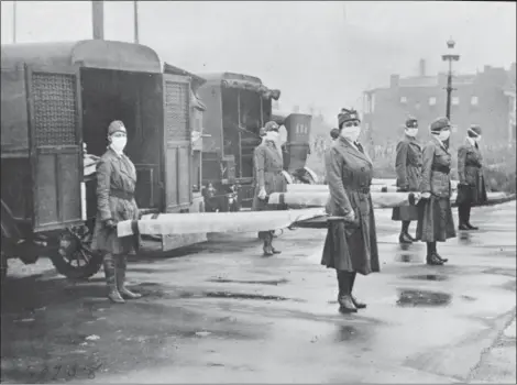  ?? LIBRARY OF CONGRESS VIA AP ?? In this October 1918 photo made available by the Library of Congress, St. Louis Red Cross Motor Corps personnel wear masks as they hold stretchers next to ambulances in preparatio­n for victims of the influenza epidemic. A century after one of history’s...