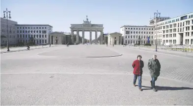  ?? ODD ANDERSEN / AFP VIA GETTY IMAGES ?? An couple walks across the deserted Pariser Platz by the Brandenbur­g Gate in Berlin on Monday.