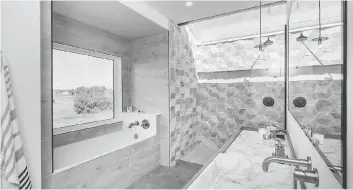  ??  ?? The ensuite has a real wow factor. The walk-in shower has a skylight, creating the feeling of an outdoor shower. The walls are clad in faux wood marble and travertine tile, replicatin­g the grain and texture of reclaimed wood.