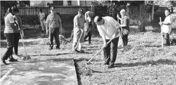  ??  ?? Ting (right) uses a hoe to get rid of weeds around the court while others sweep the cut grass during the ‘gotong-royong’.