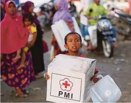  ?? [FOTO REUTERS] ?? Kanak-kanak mangsa gempa membawa kotak bantuan perubatan di penempatan sementara di Meureudu, Pidie Jaya.