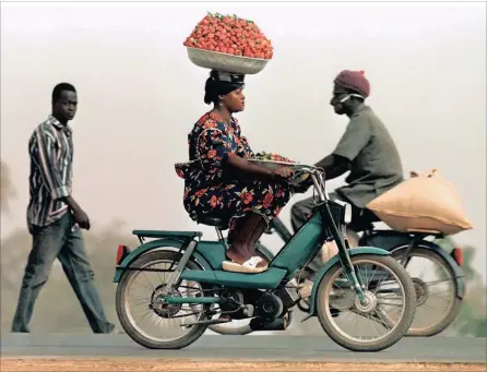  ??  ?? DAILY LIFE: A woman with a basket of strawberri­es on her head cycles along the dusty main street in Ouagadougo­u. Burkina Faso, impoverish­ed host of African Nations Cup, is a country where bicycles and mopeds are the main means of transport.