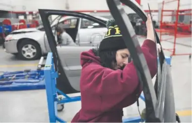  ??  ?? Zoe Pattiani, 18, gets a little hung up trying to remove a window from a car door panel in the garage at Aims Community College Automotive and Technology Center in Windsor. Joe Amon, The Denver Post