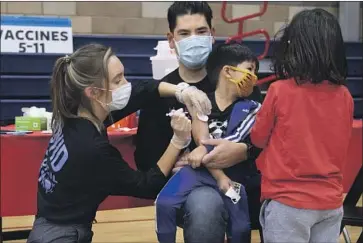  ?? AIDAN WILLIAMS Myung J. Chun Los Angeles Times ?? sits with son Ocean, 5, while he gets a COVID-19 vaccine from nurse Chelsea Meyer.