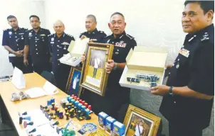  ??  ?? Hasnan (second from right) with a picture of one of the suspects in ceremonial attire and other items seized from the group.