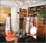  ??  ?? A man and a woman demonstrat­e dining under a plastic shield Wednesday in a restaurant of Paris