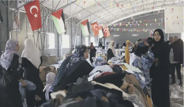  ??  ?? 0 Palestinia­n residents choose pieces of clothing from a Turkish aid shipment in Gaza City. The goods have begun arriving through the border crossing with Israel to Gaza