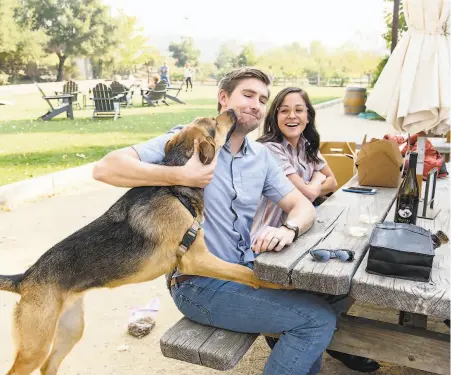  ??  ?? Conor McLaughlin gets a kiss from his dog, Ava, as he and Paige McLaughlin sip wine at Imagery Estate Winery in Glen Ellen.