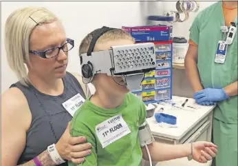  ??  ?? Brody Bowman, 6, plays virtual-reality games while getting a medication infusion at Nationwide Children’s Hospital. His mother says he barely reacts to needle pricks while distracted by the games, which it makes the treatment process much easier on...