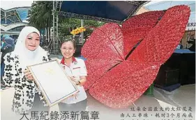  ??  ?? 這朵全國最大的大紅花­是由人工串珠，耗時3個月而成的。左起為Arena創意­私人有限公司的創始人­阿斯法莉娜及大馬紀錄­辦公室經理李佩玲。