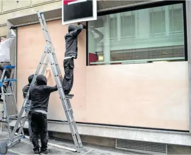  ?? Foto: Efe ?? Varios hombres instalan paneles de madera en una tienda de los Campos Elíseos de París.