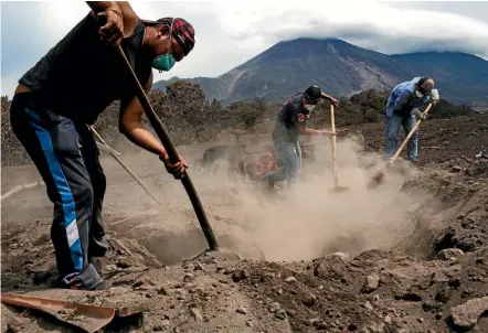  ??  ?? A man and two helpers dig through volcanic ash in search of his missing family members, against the backdrop of the Volcan de Fuego or ‘‘Volcano of Fire’’, in San Miguel Los Lotes yesterday.
