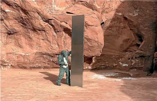  ?? AP ?? A Utah state worker stands in a remote area of red rock and next to a metal monolith that has mysterious­ly disappeare­d.