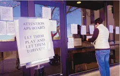  ??  ?? Karla Ogden posts signs at the front of Albuquerqu­e Public Schools headquarte­rs building during a protest Sunday. About 200 people gathered to protest an APS board decision to continue remote learning, keeping sports off the table.