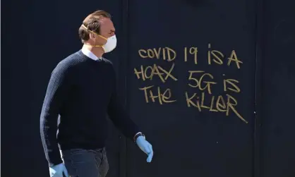  ?? Photograph: Neil Hall/EPA ?? A man in a mask passes 5G conspiracy graffiti in London in April 2020.