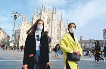  ?? ANDREAS SOLARO AFP VIA GETTY IMAGES ?? Women wearing respirator­y masks walk across Piazza del Duomo near Milan Cathedral on Sunday. Ten towns in Italy’s Lombardy region are on lockdown after coronaviru­s cases emerged in Codogno, southeast of Milan.