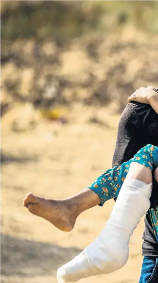  ??  ?? A girl injured by a mortar in Ras al-ain, northeaste­rn Syria, is carried away after having her leg bandaged, right. Below, Syrian Kurds protest against the Turkish assault in the town of Qamishli