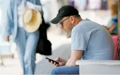  ??  ?? Geoff Hunnicutt of Portland, Ore., uses his cellphone under the portal on Palace Avenue earlier this month. The cellphone service by Verizon in the downtown area has declined, but Hunnicutt, who uses AT&T, said, ‘I’ve got full bars, I haven’t noticed a...