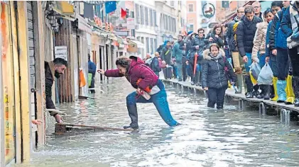  ??  ?? Cola para cruzar. Vecinos y turistas esperan para sortear el agua en un sector muy afectado de Venecia.Oficinas