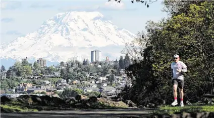  ?? BRIAN HAYES bhayes@thenewstri­bune.com ?? A runner jogs along the Ruston Way Path as Mount Rainier looms through the partly cloudy skies on May 8 in Tacoma. .