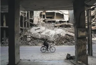  ?? Sameer Al-Doumy / AFP / Getty Images ?? A man cycles past destroyed buildings in the rebel-held town of Douma, on the eastern outskirts of Damascus. Fighting subsided in Syria after a deal to create safe zones took effect.