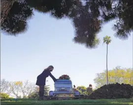  ?? Christina House Los Angeles Times ?? CLARICE KAVANAUGH places a hand on the casket of Charles “Chuck” Jackson, her close friend who died of COVID- 19, at Inglewood Park Cemetery in April.