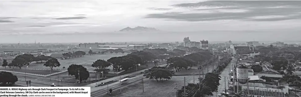  ?? GABRIEL MURAD | DREAMSTIME.COM ?? MANUEL A. ROXAS Highway cuts through Clark Freeport in Pampanga. To its left is the Clark Veterans Cemetery. SM City Clark can be seen in the background, with Mount Arayat peeking through the clouds.