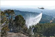  ??  ?? A helicopter drops water on a brush fire in Oakland, Calif., last summer. Federal officials hope one day unmanned aircraft can do the job.