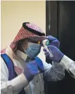  ?? ?? Saudi volunteers check each other’s temperatur­es using an electronic thermomete­r