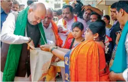  ?? — PTI ?? BJP President Amit Shah collects foodgrains from a farmer family during a doorto-door campaign Mushti Dhanya Sangrah Abhiyana, ahead of Karnataka Assembly Elections at Doddabathi village in Davanagere on Tuesday.