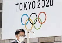  ?? KOJI SASAHARA/AP ?? A man wearing a mask walks in front of an Olympics logo at the Tokyo metropolit­an government headquarte­rs building Wednesday.