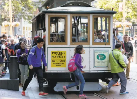  ?? Photos by Paul Chinn / The Chronicle ?? Passengers dash to seize a prime outside spot on a Powell-Mason car at the cable-car turnaround at Powell and Market streets.