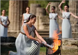  ?? AP PHOTO/THANASSIS STAVRAKIS, FILE ?? FILE - Greek actress Xanthi Georgiou, playing the role of the High Priestess, lights the torch during the lighting of the Olympic flame at Ancient Olympia site, birthplace of the ancient Olympics in southweste­rn Greece Oct. 18, 2021.