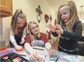  ??  ?? Skylar, 17, center, helps her younger sisters Anna, 4, left, and Charlie, 3, with arts and crafts at their home. The older adopted siblings help care for the younger ones to help them adjust.