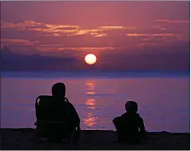  ?? WILFREDO LEE / AP FILE ?? A pair of beach goers watch the sun rise over the Atlantic Ocean on June 10 in Surfside, Fla. All the experts predicted this would be a more active than normal hurricane season, but then nothing happened. Scientists think a persistent patch of dry air is the reason storms aren’t forming.